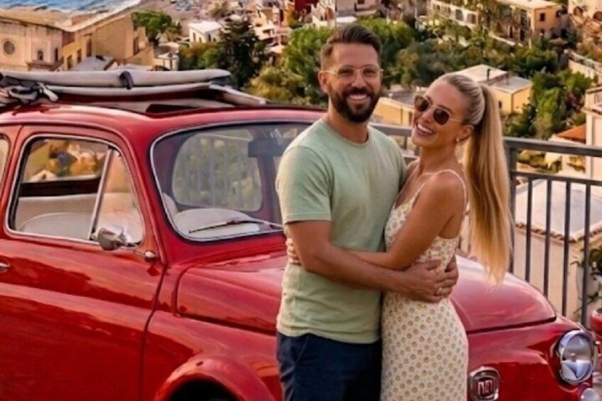 Un couple s’embrasse devant une voiture rouge ancienne, avec une vue sur la ville en arrière-plan. 1