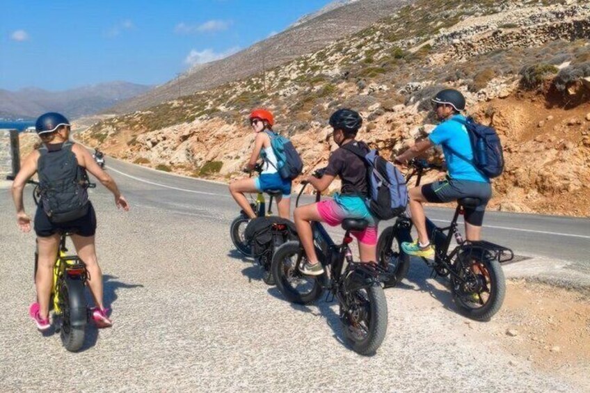 Quatre personnes font du vélo électrique sur une route asphaltée, avec un paysage montagneux en arrière-plan. 1