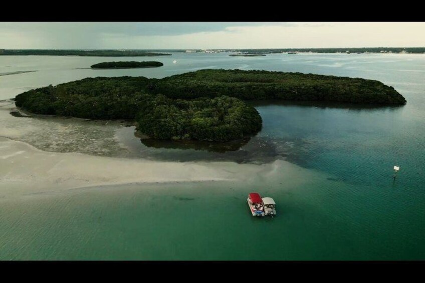 Vista aerea di un'isola tropicale con acque turchesi cristalline, circondata da piccoli isolotti, e una barca ancorata vicino alla riva. 2