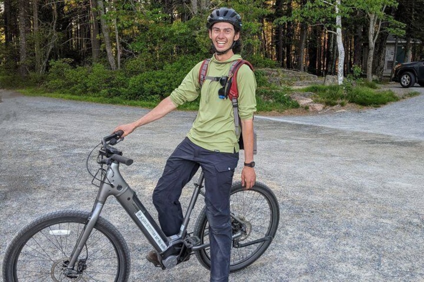 A person standing next to a mountain bike on a gravel path with trees in the background. 3