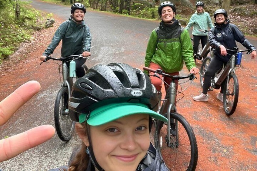 A group of cyclists on a paved path surrounded by trees. 1
