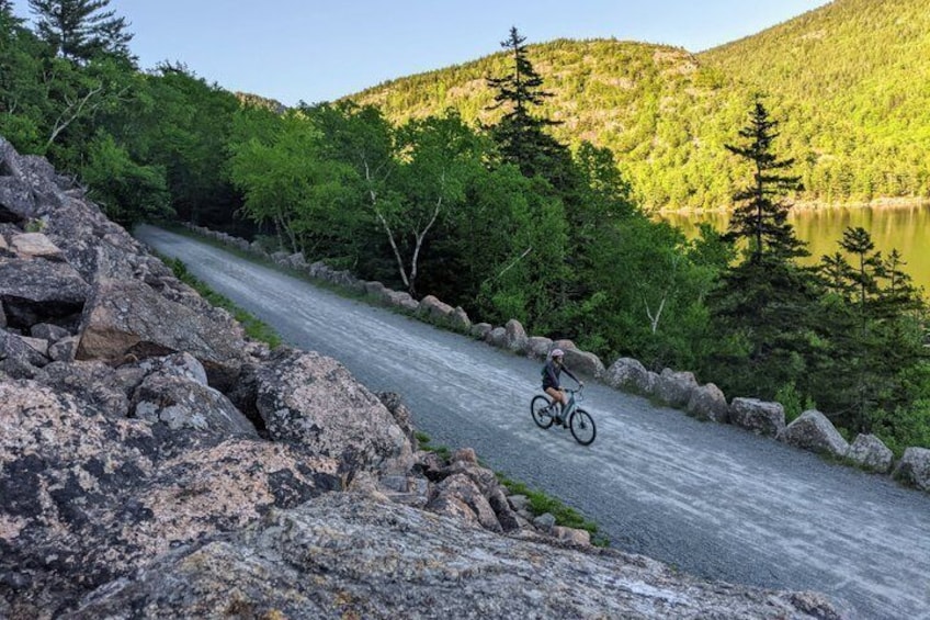 A cyclist on a paved road surrounded by rocky terrain and dense forest. 2