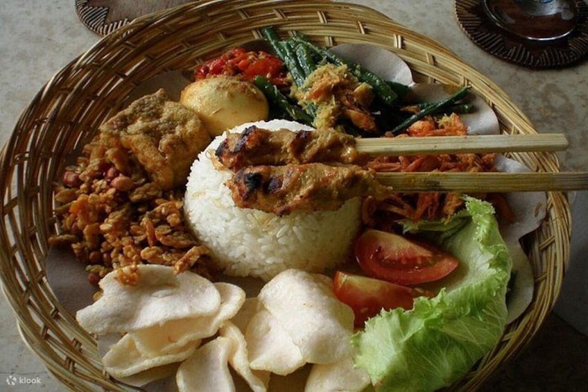 Eine traditionelle indonesische Mahlzeit mit Reis, Hähnchen, Gemüse und frittierten Speisen in einem gewebten Korb. 3