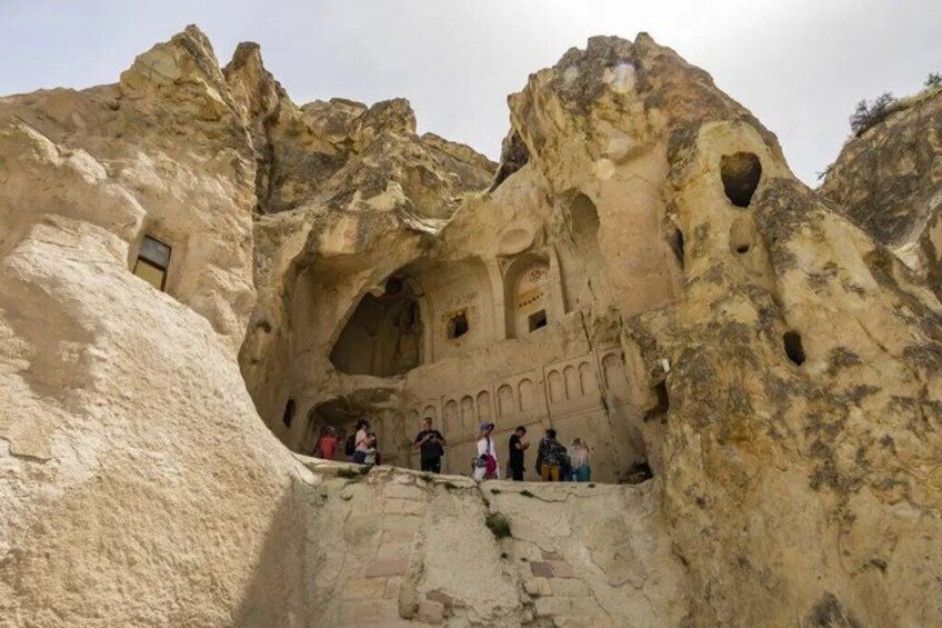A rock formation with carved niches and a group of people standing on a ledge. 5