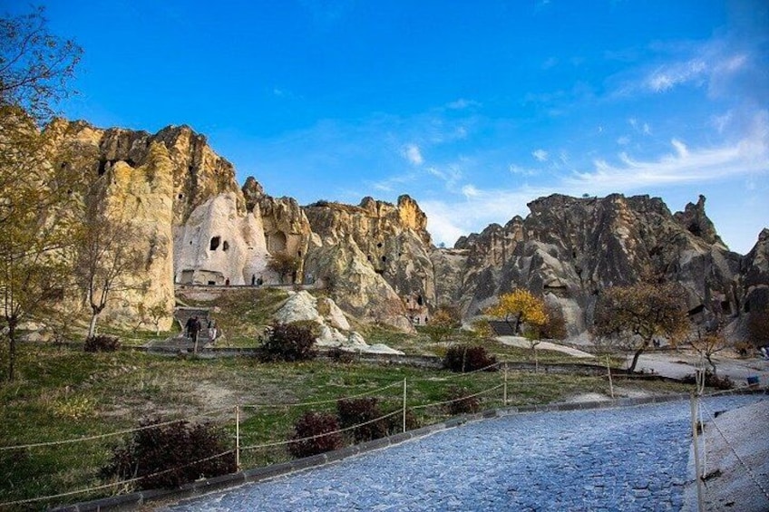 A rocky landscape with a cave entrance, trees, and a clear sky. 3