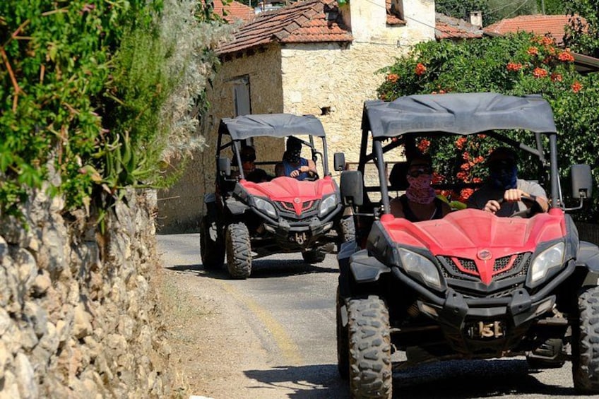Two red off-road vehicles on a narrow road with stone walls and vegetation on the sides. 5
