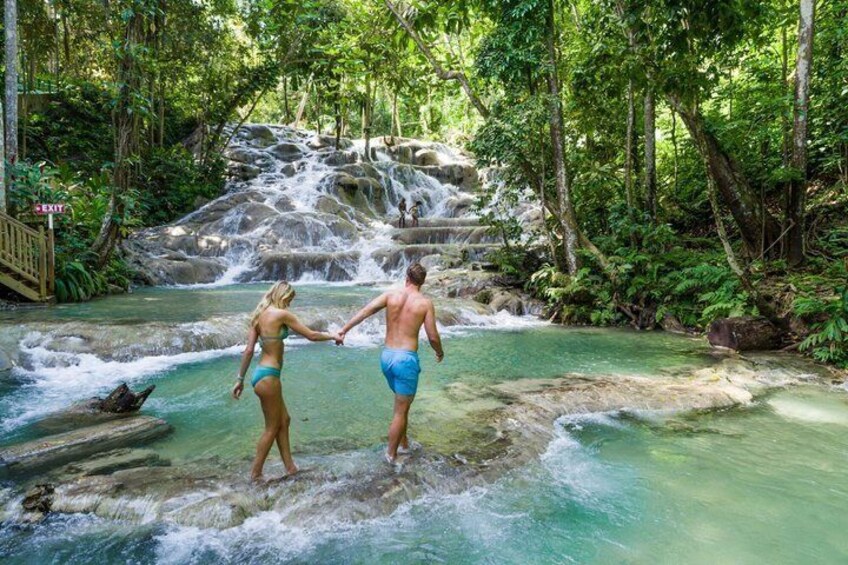 A couple holding hands by a clear water stream with a waterfall in the background. 5