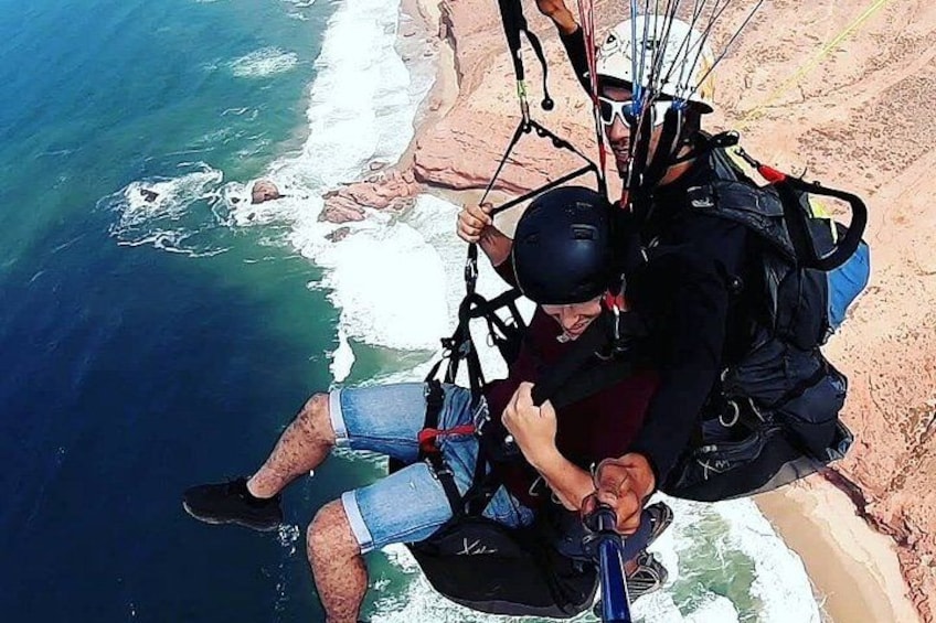 A person paragliding over a coastal cliff with ocean waves below. 1