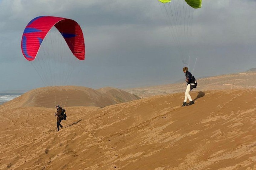 A person paragliding over a desert landscape with sand dunes and a cloudy sky. 5