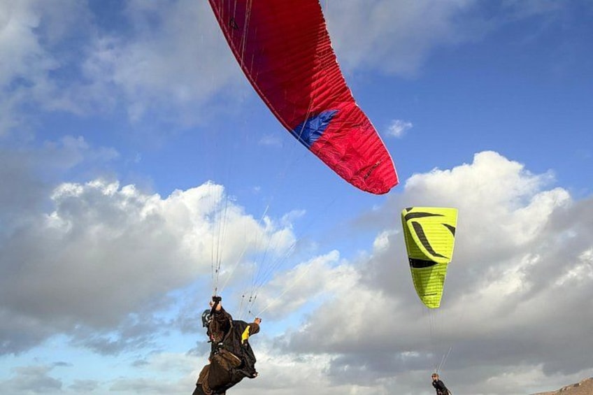 A person paragliding with a red and yellow parachute against a cloudy sky. 4