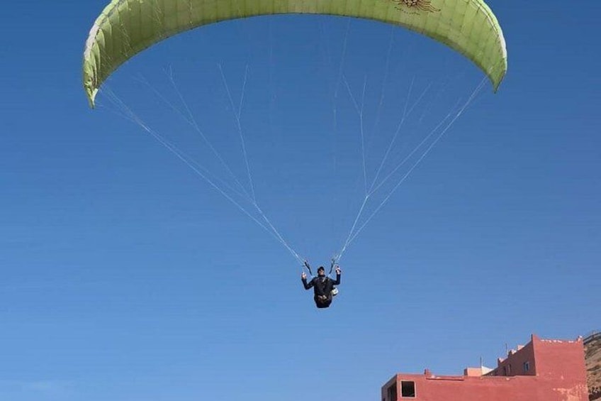 A paraglider with a green canopy flying against a clear blue sky. 2