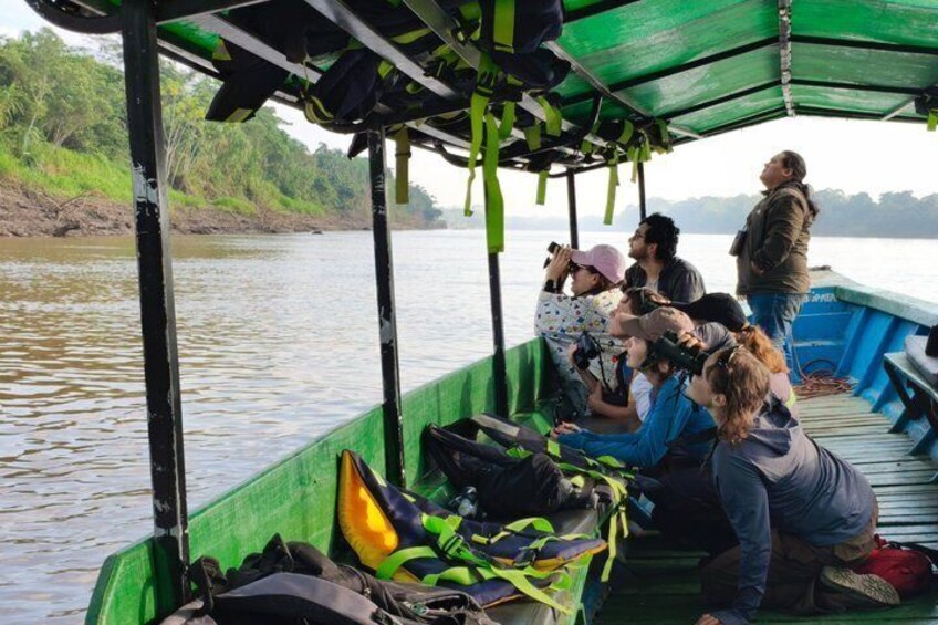 Un bote verde con gente a bordo, algunas personas tomando fotografías, y un río al fondo. 4