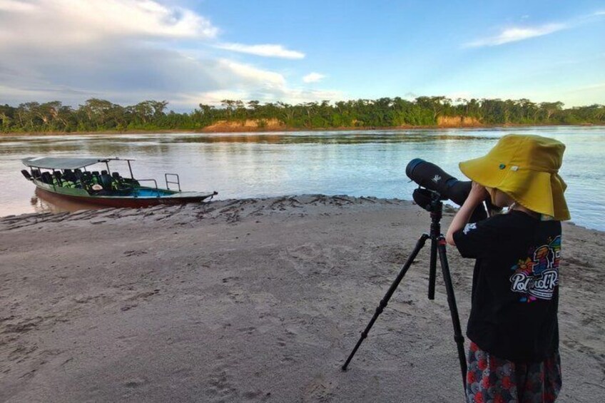 A boat on a sandy shore, a person with a telescope, and a river with trees in the background. 4