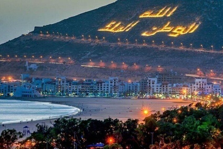Una spiaggia con edifici e una collina con iscrizioni arabe illuminate. 3