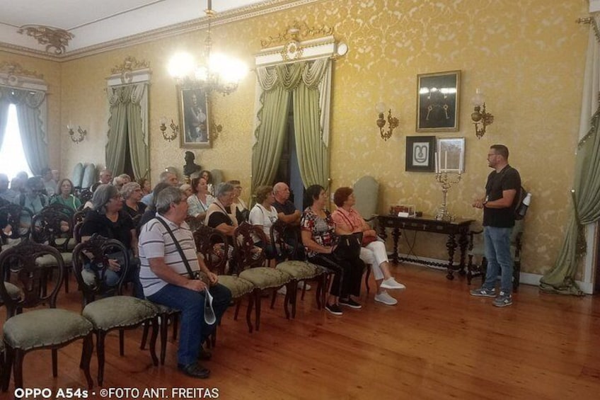 Un incontro formale in interni, con persone sedute e in piedi, un lampadario e decorazioni murali elaborate. 4