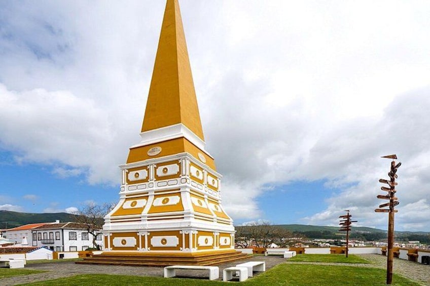 Un monumento alto e giallo con decorazioni bianche, circondato da un'area erbosa e con edifici sullo sfondo. 2