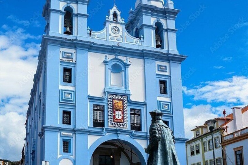Un edificio in stile coloniale blu con una torre dell'orologio e una statua di fronte, con un tricolore rosso. 1