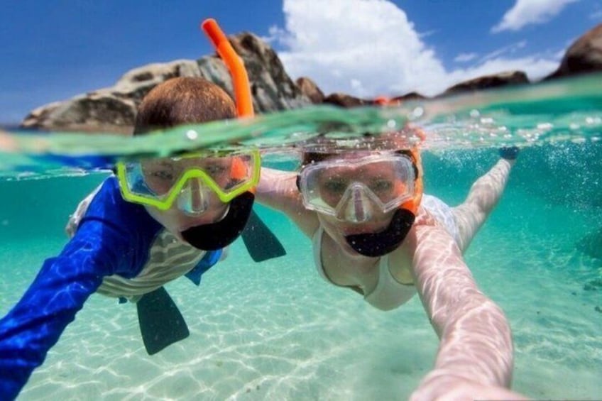 Two people snorkeling underwater with clear turquoise water and rocky formations in the background. 5