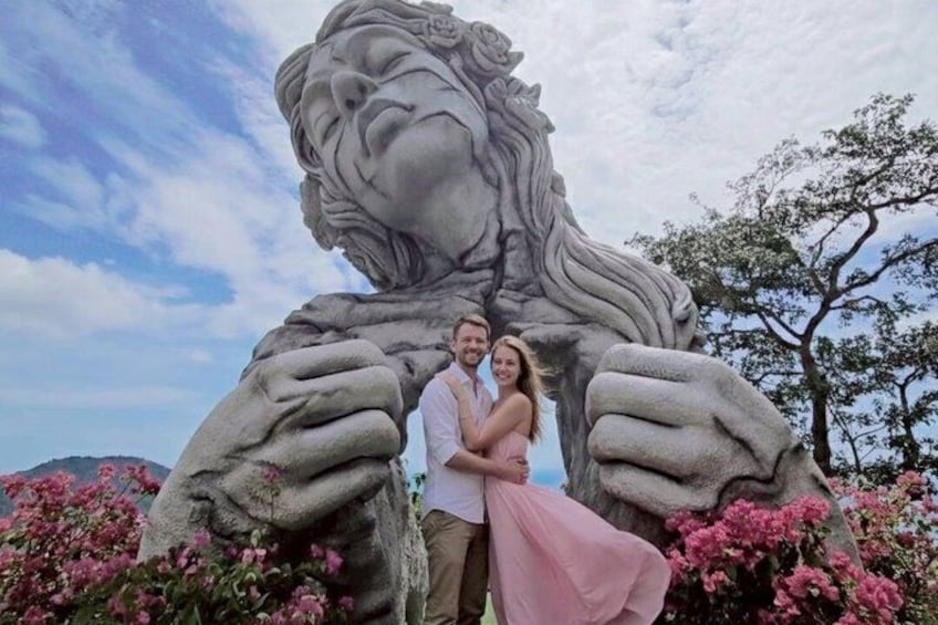 A couple standing in front of a stone lion statue with pink flowers in the foreground. 4