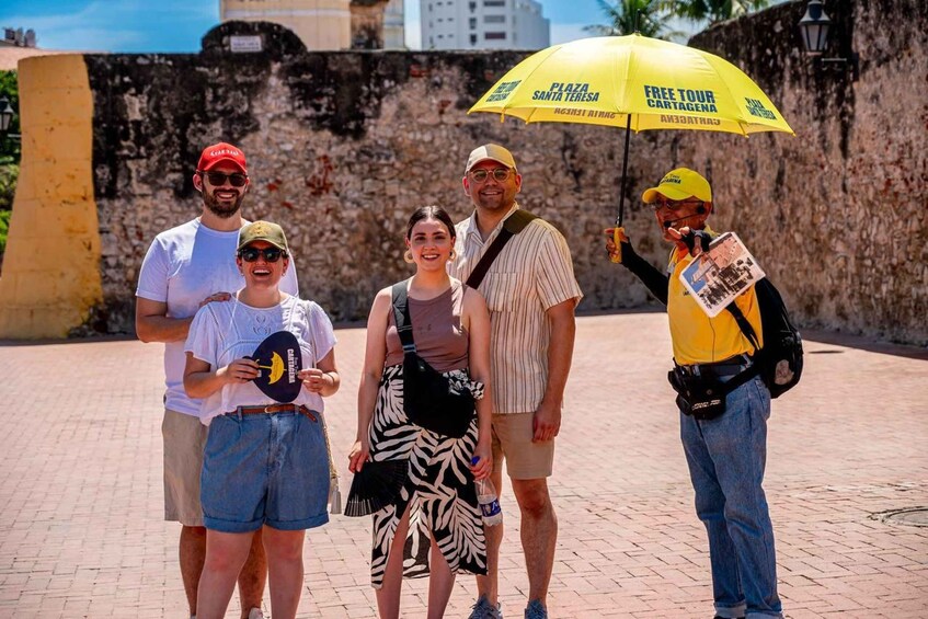 A group of people standing on a paved area with a stone wall in the background. 5