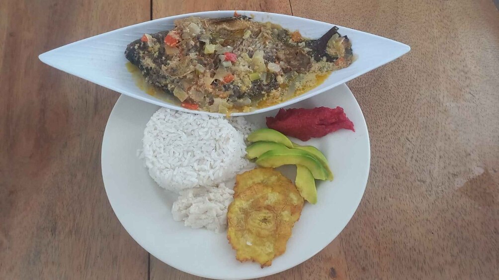 A plate with white rice, fried plantains, sliced avocado, red meat, and a fish dish with vegetables. 3
