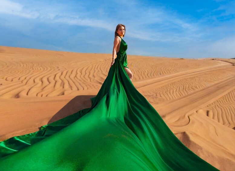 A person in a green dress standing on a sand dune with rippled patterns. 4