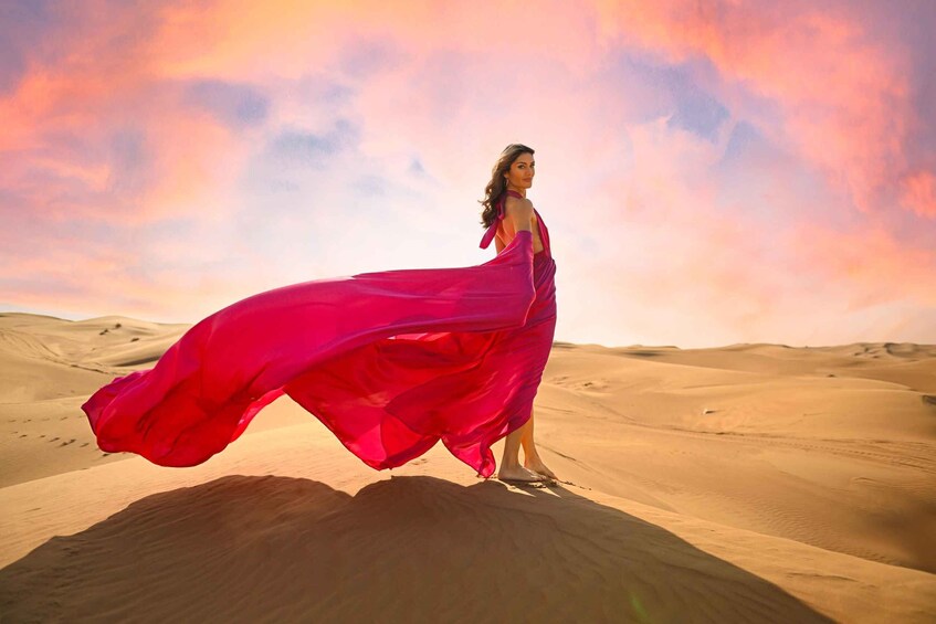 A person in a flowing pink dress standing on a sand dune with a desert landscape in the background. 3