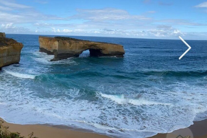 Un paysage côtier avec une grande formation rocheuse s’élevant en arc au-dessus de la mer et une plage de sable. 3
