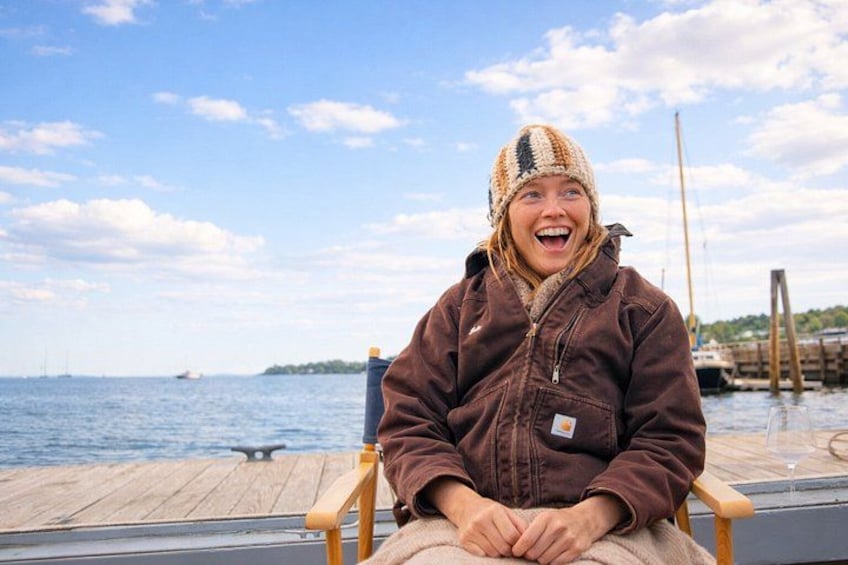 A person sitting on a wooden chair by a dock with a body of water and boats in the background. 3
