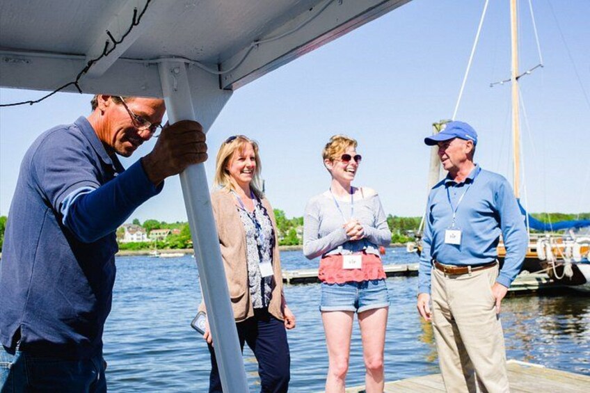 A group of people on a boat near a dock with water and buildings in the background. 5