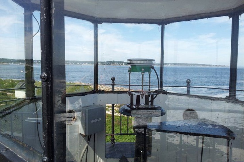 Una estructura de faro con un cerramiento de cristal, un accesorio de luz verde y vistas al mar. 3