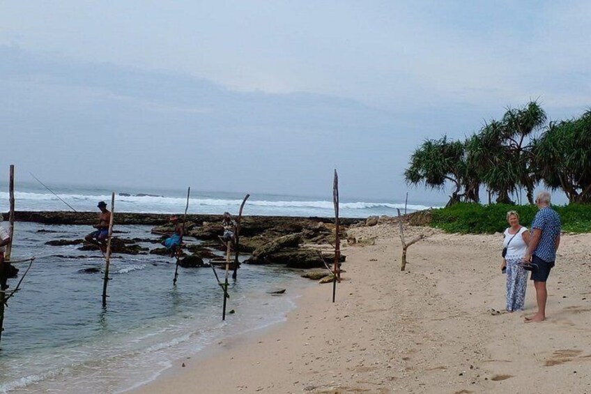 A beach with people fishing, a rocky shoreline, and a tree line. 3