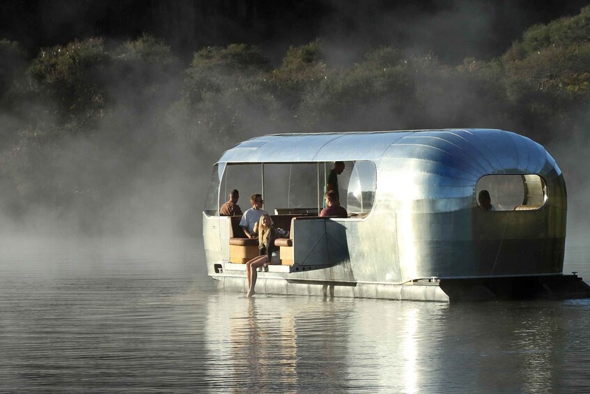 A stationary boat with passengers on a calm body of water, surrounded by mist and dense vegetation. 1