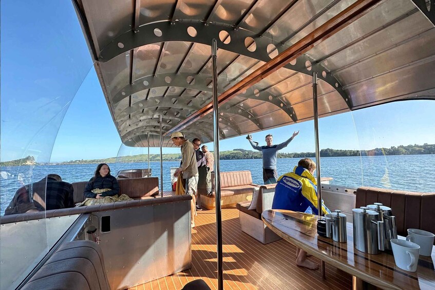 A boat with people on deck, a covered area with a metal roof, and a body of water in the background. 3