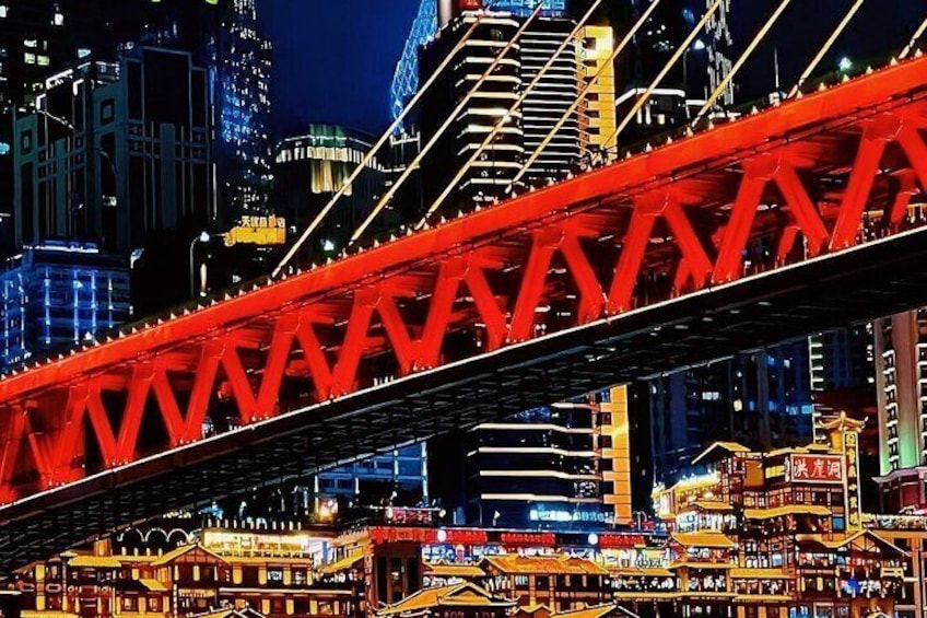 A red bridge over a cityscape at night with illuminated buildings and signs. 1