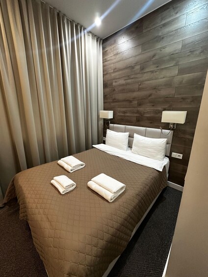 A hotel room with a brown quilted bedspread, white pillows, and two folded towels on the bed. 5