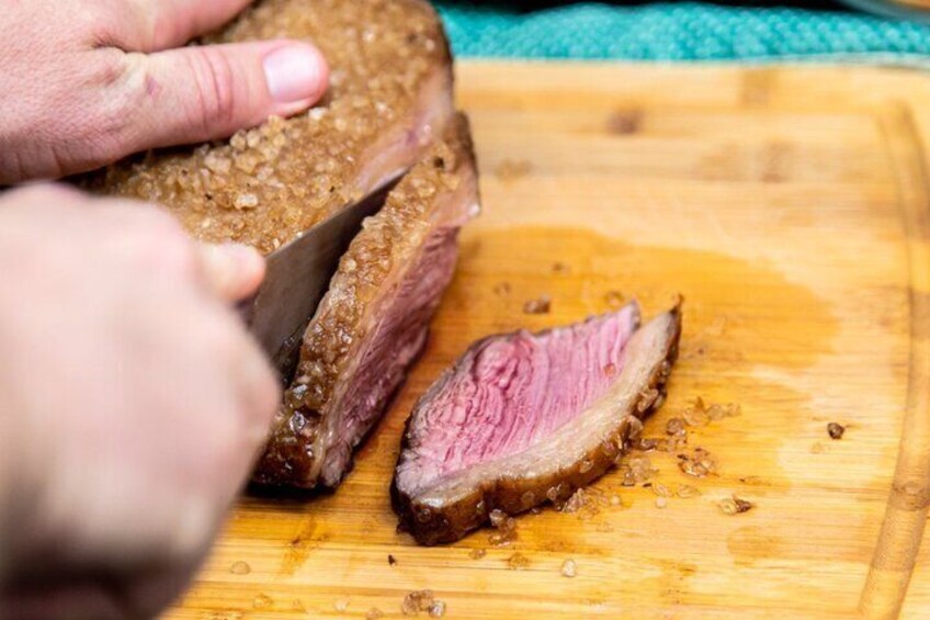 A person slicing a piece of meat on a wooden cutting board. 2