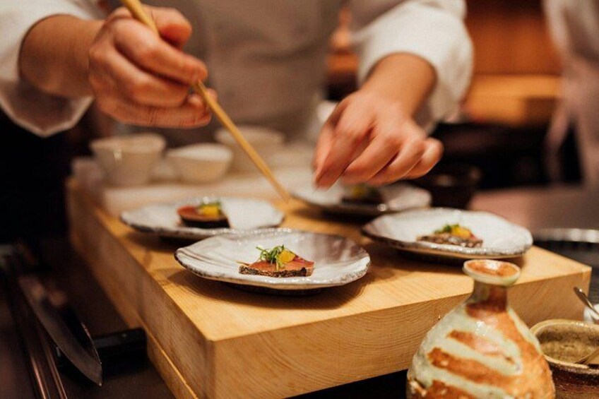 Un chef preparando comida sobre una encimera de madera, con platos de comida y una botella de salsa. 2
