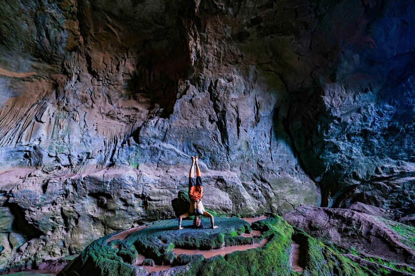 A person performing a handstand on a moss-covered rock in a cave. 4