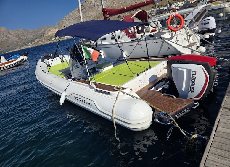 A white inflatable boat named ICON 28 docked at a marina with a blue canopy, a green deck, and an outboard motor labeled EVINRUDE. 2
