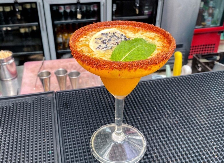 A margarita cocktail with a salted rim, garnished with a slice of lime and a leaf, on a bar counter. 2