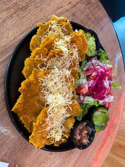 A plate with fried plantains, guacamole, a salad, and a lime wedge. 5