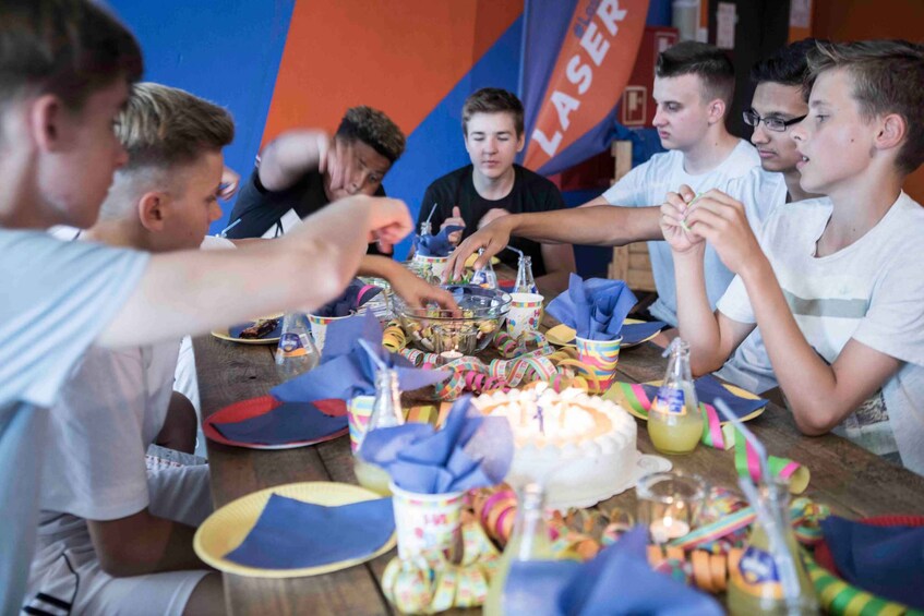 A group of people around a table with a cake, drinks, and party decorations. 3