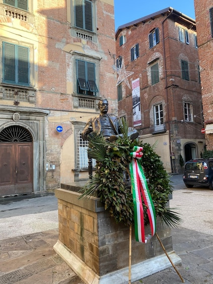 A statue with a wreath and a flag on a pedestal in front of a building. 3