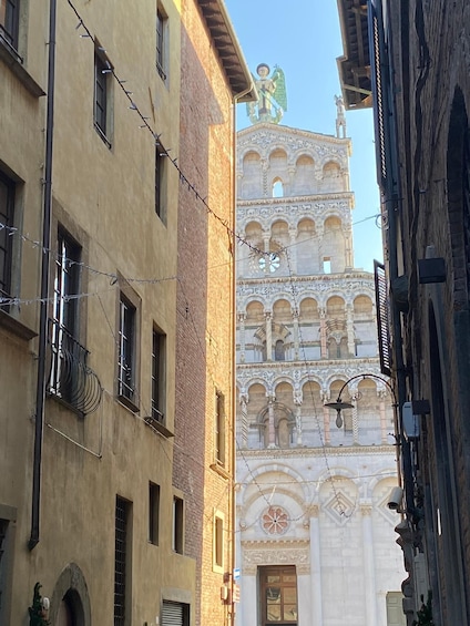 A narrow street with buildings, a decorative tower, and a statue. 1