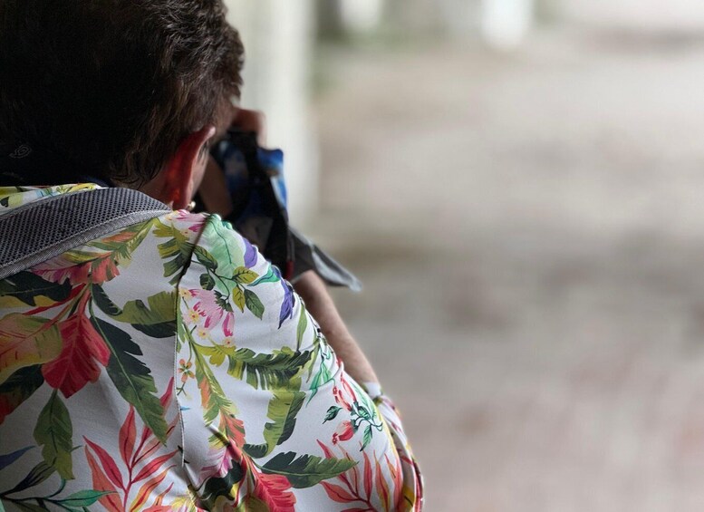 Iemand in een bloemenhemd, een camera vasthoudend, met een vage achtergrond. 2