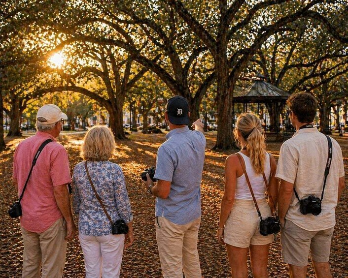 Een groep mensen staat in een park met bomen en een kiosk op de achtergrond. 5