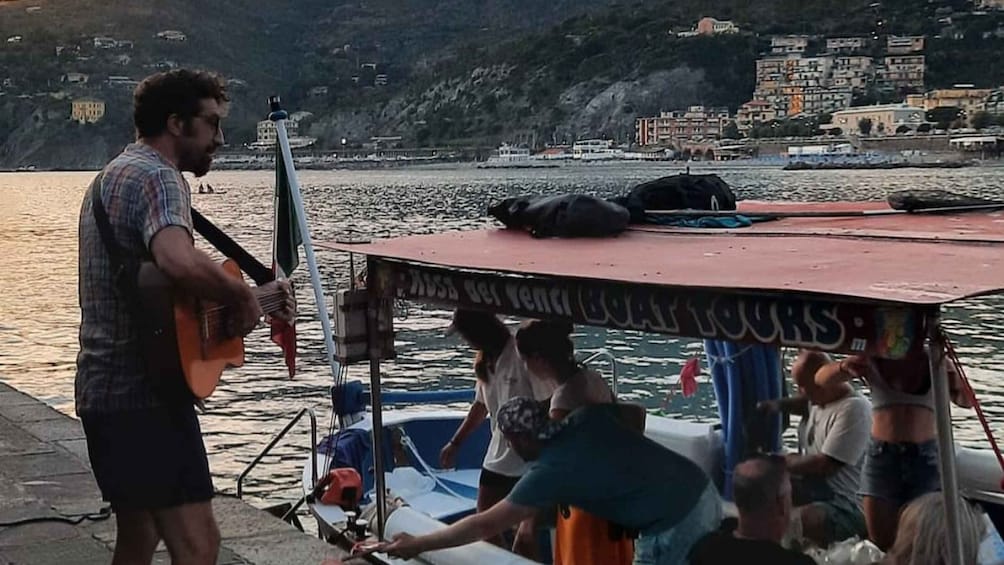 A musician playing guitar on a boat with a group of people. 3