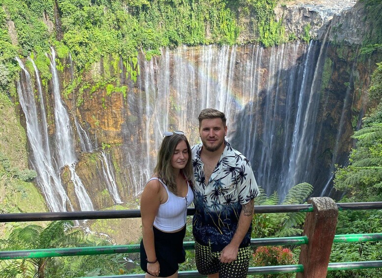 A couple standing in front of a multi-tiered waterfall with lush greenery in the background. 4