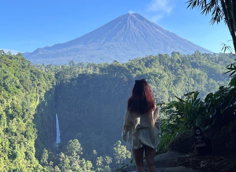 A woman standing with a view of a volcano and a waterfall. 3